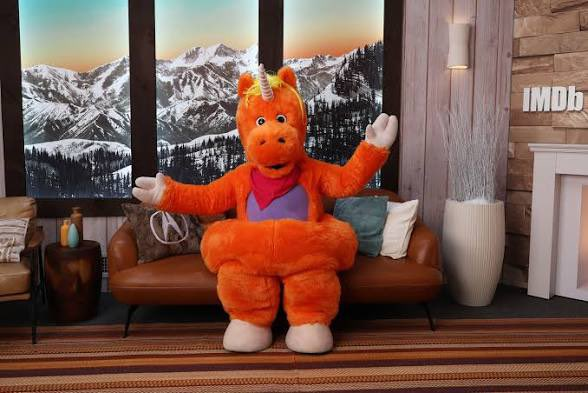 Buddy sitting on a sofa with arms open in a mountain lodge.